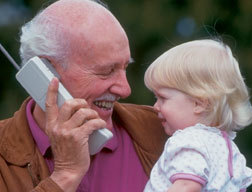 picture of an older man holding a phone, gazing at a little girl in his arms